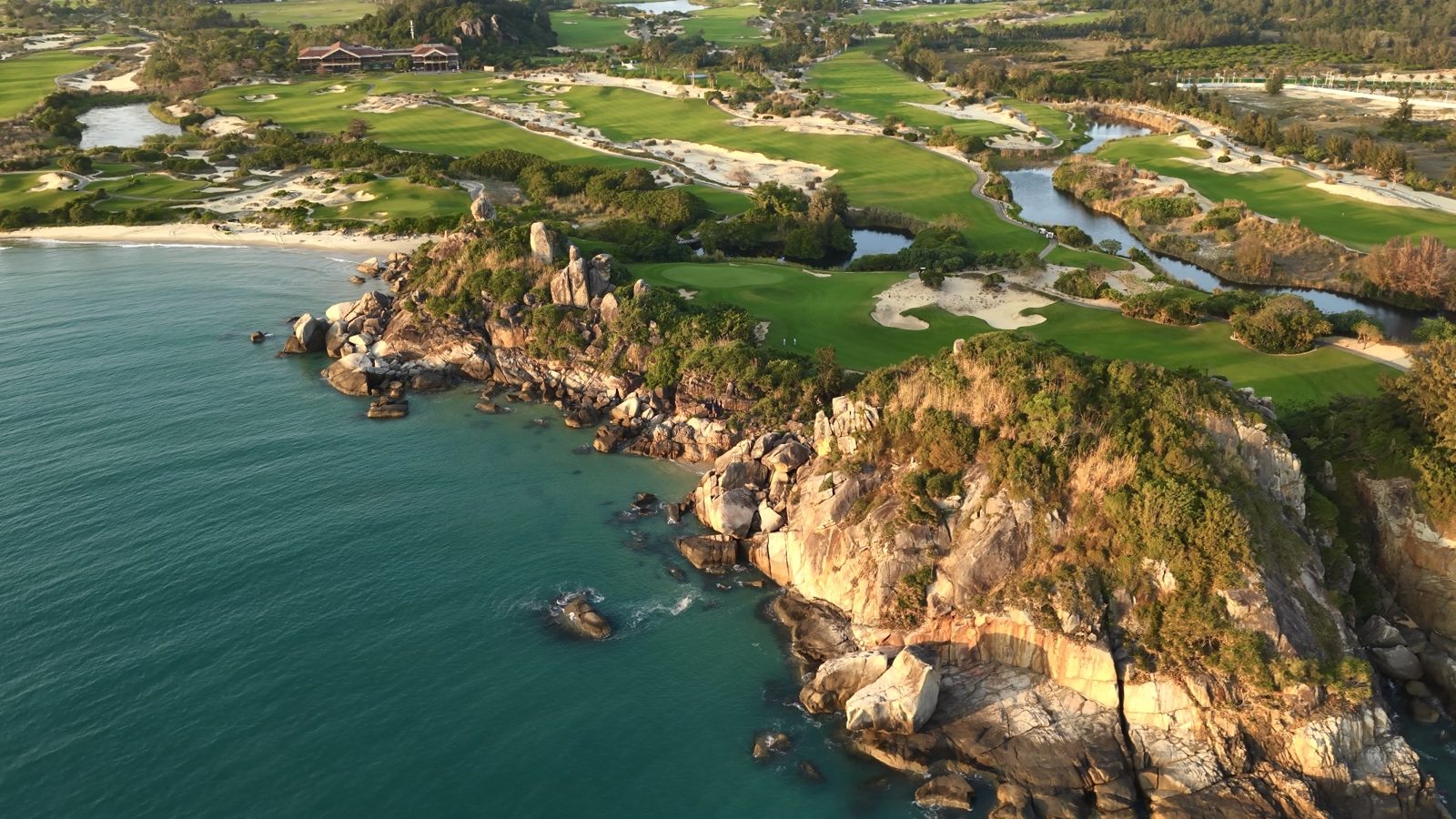 An aerial view of The Dunes wrapping a rocky headland above a turquoise bay at Shenzhou Peninsula