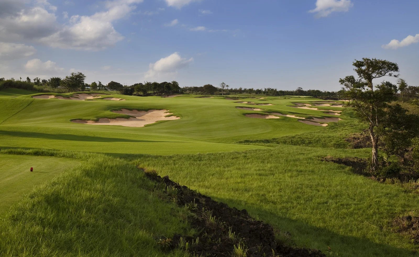 The wide 14th fairway at Lava Fields, Mission Hills Haikou, dotted with sand bunkers