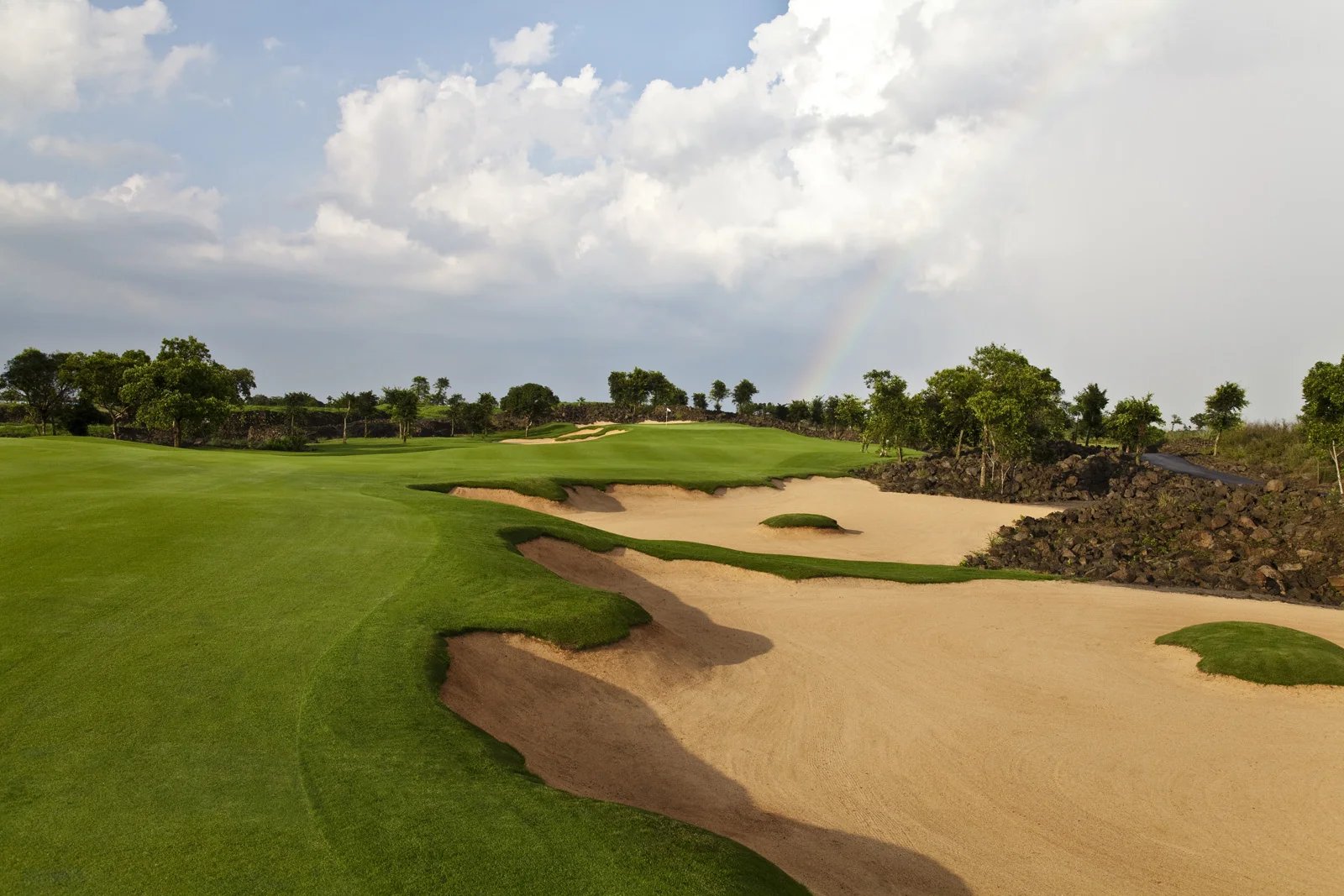 A rainbow over the 5th hole at Lava Fields, sand waste and lava rock beside the fairway