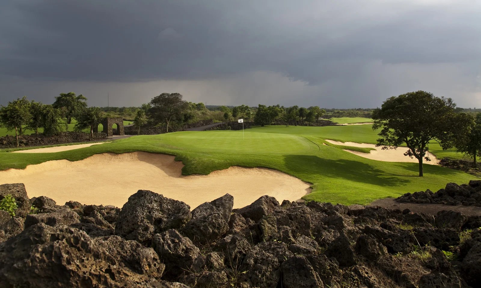 The 5th green at Lava Fields, Mission Hills Haikou, framed by black lava rock under a storm sky
