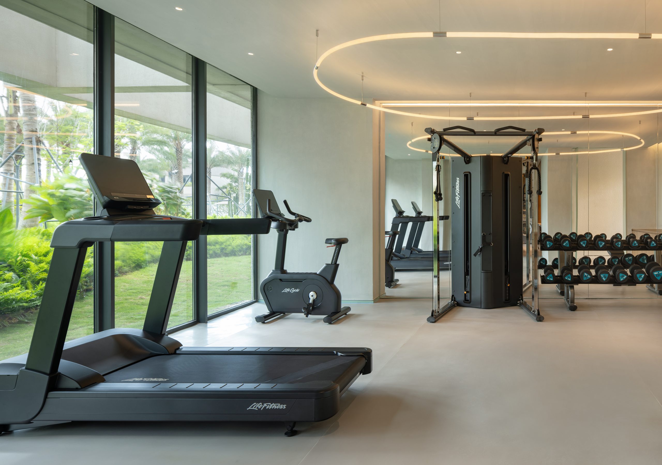 Hotel gym with treadmill, bike and cable machine looking onto the gardens at the surf resort inside the Riyue Bay wave pool grounds, Wanning, Hainan — stay paddle-fit between wave pool sessions