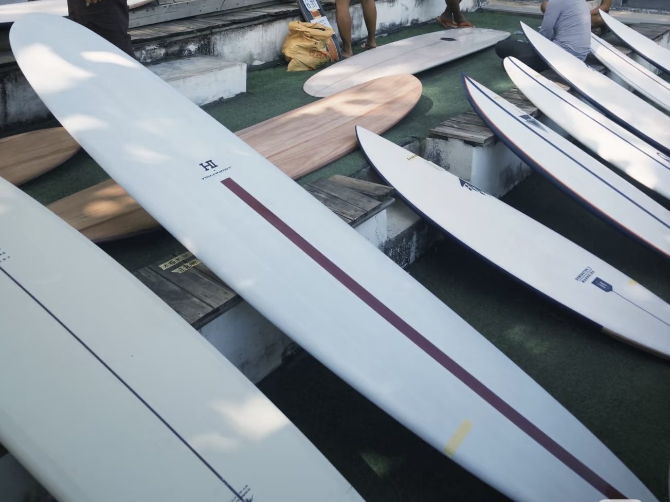 Rental surfboards lined up on the rack at the Riyue Bay surf shop, Wanning, Hainan — shortboards and longboards for the PerfectSwell wave pool