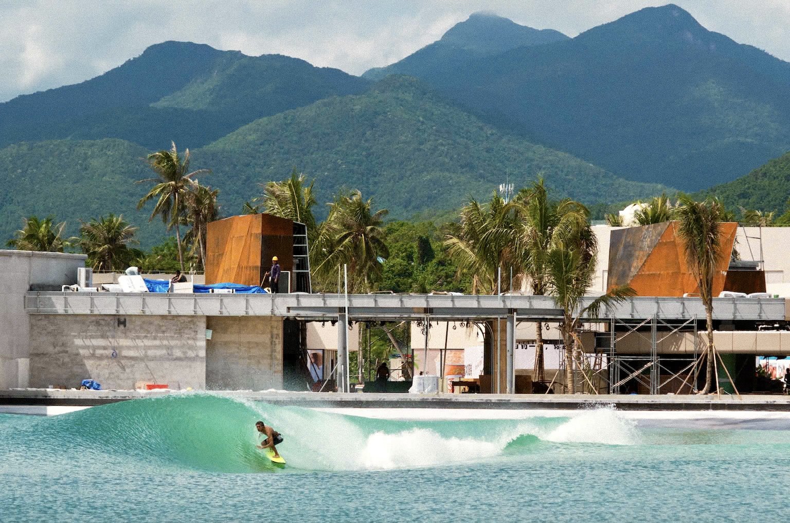Surfer riding a wave at PerfectSwell Hainan with tropical mountains and palm trees behind