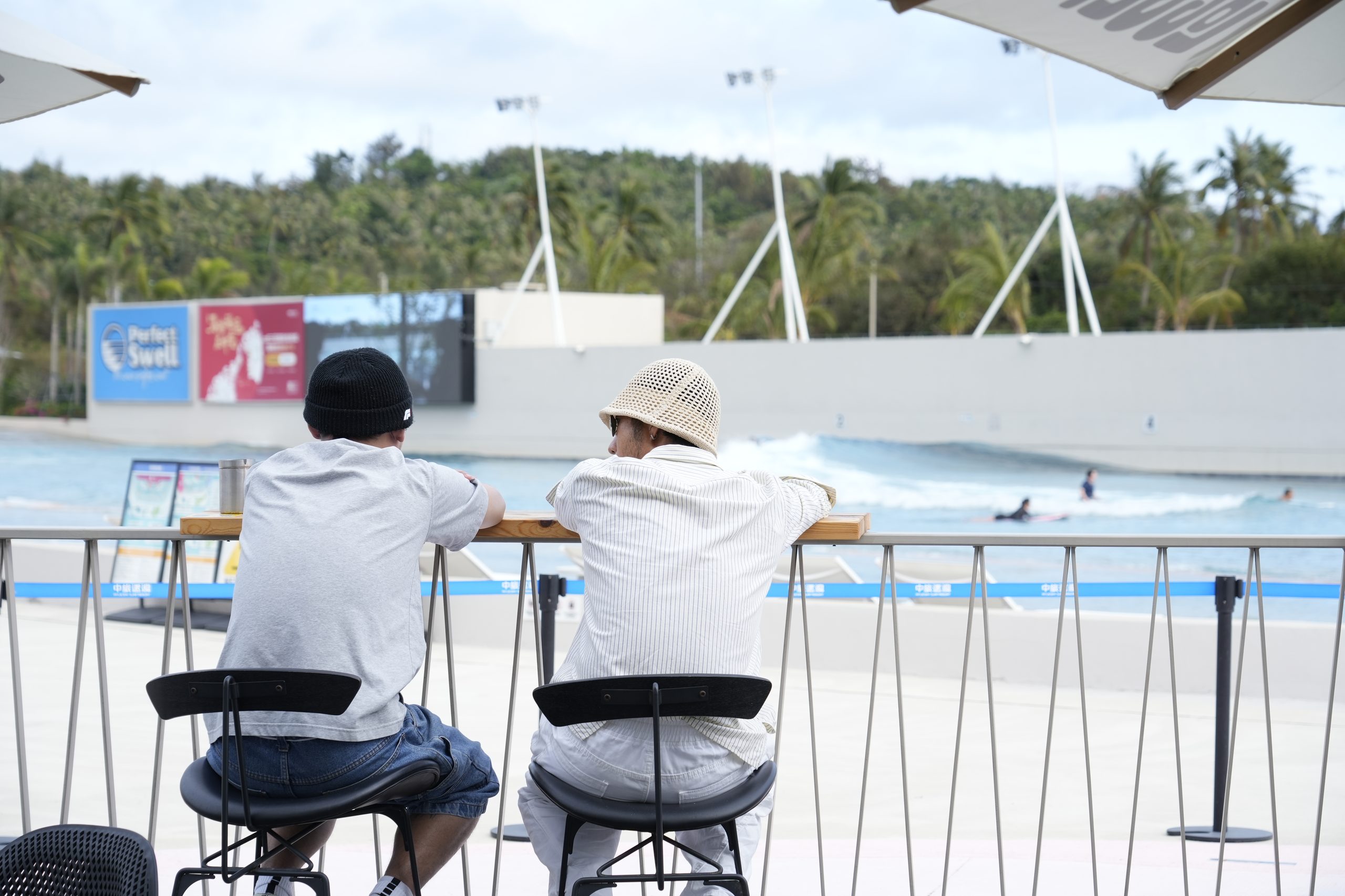 Family and friends watching surfers from the edge of the wave pool at Riyue Bay, Wanning — every wave visible from the poolside
